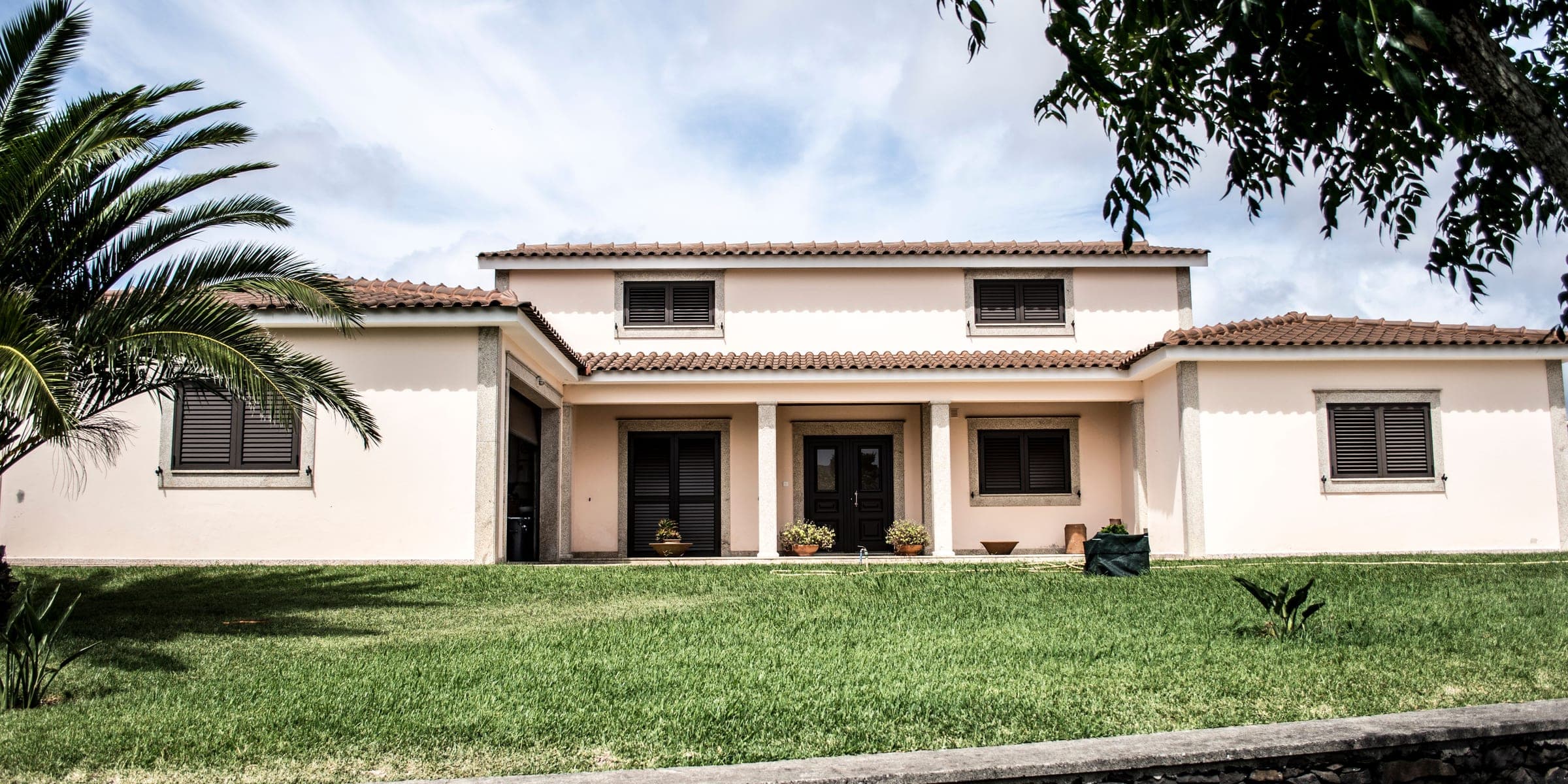 Cream two-story stucco house with a tile roof, front lawn and palm fronds