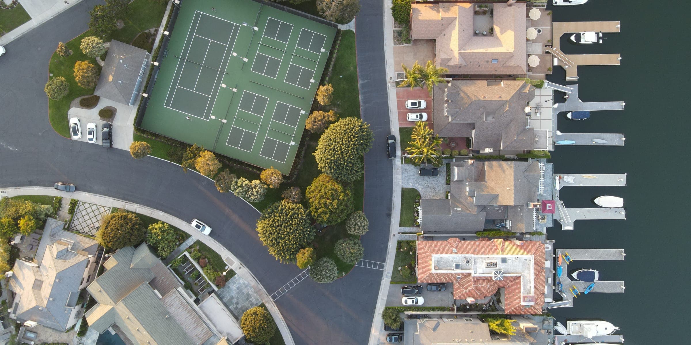 Top-down aerial view of waterfront homes with boat docks beside a tennis court
