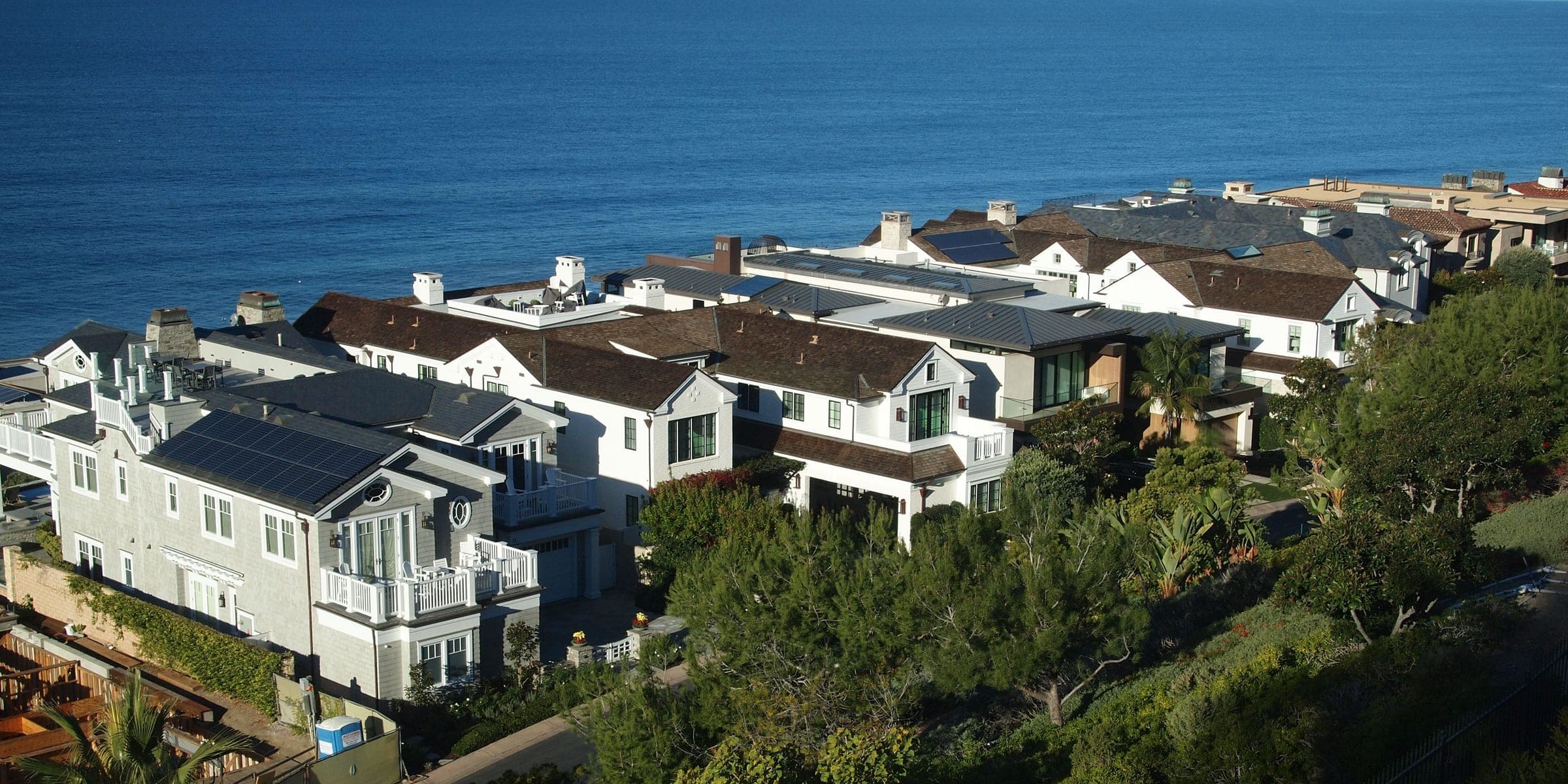 Two-story coastal homes on a bluff above the blue ocean, with trees below