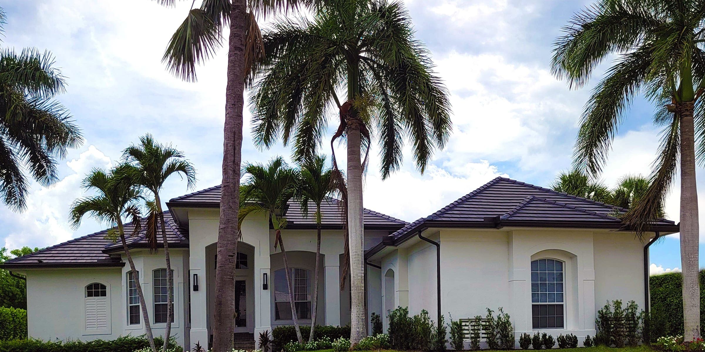 Single-story white stucco house with a tile roof, tall palm trees and a green lawn