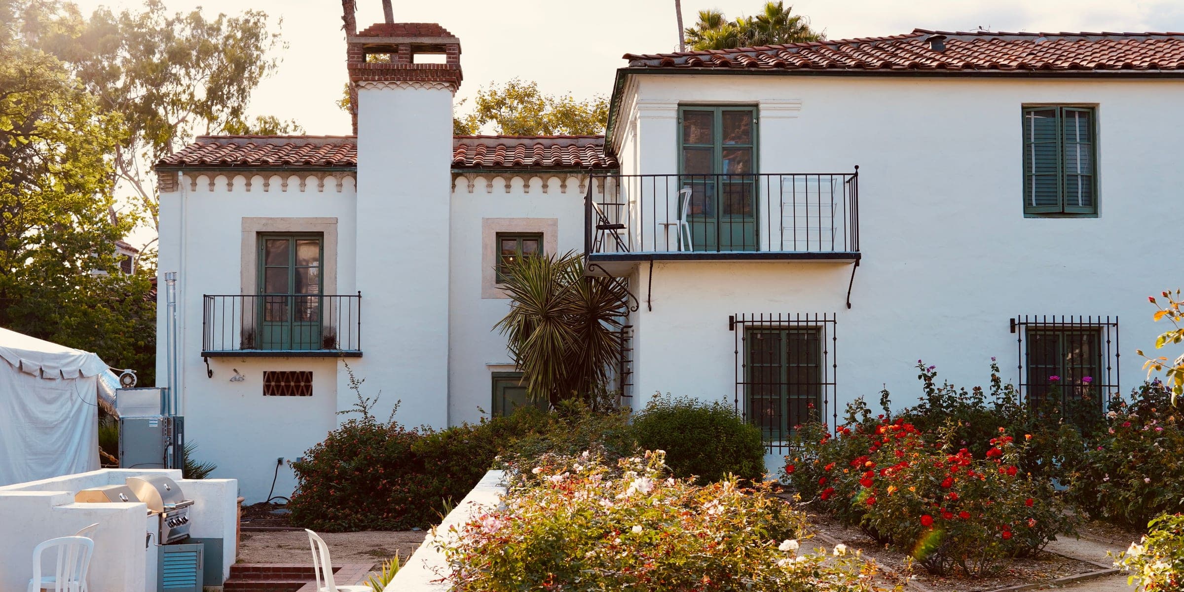 White two-story Spanish style house with a clay tile roof, iron balconies and a rose garden