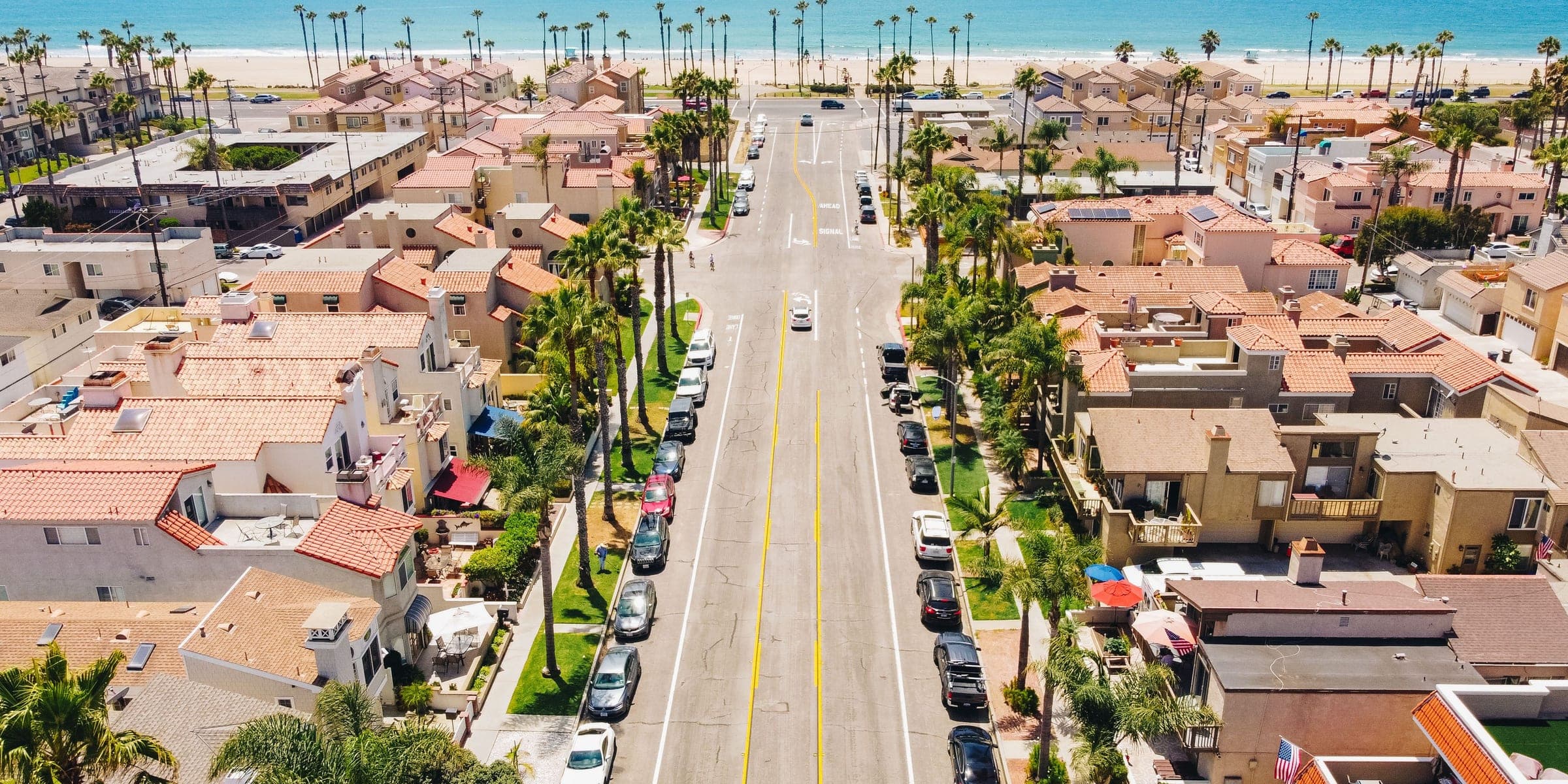 Aerial view of a palm-lined street with tile-roofed homes leading to the ocean