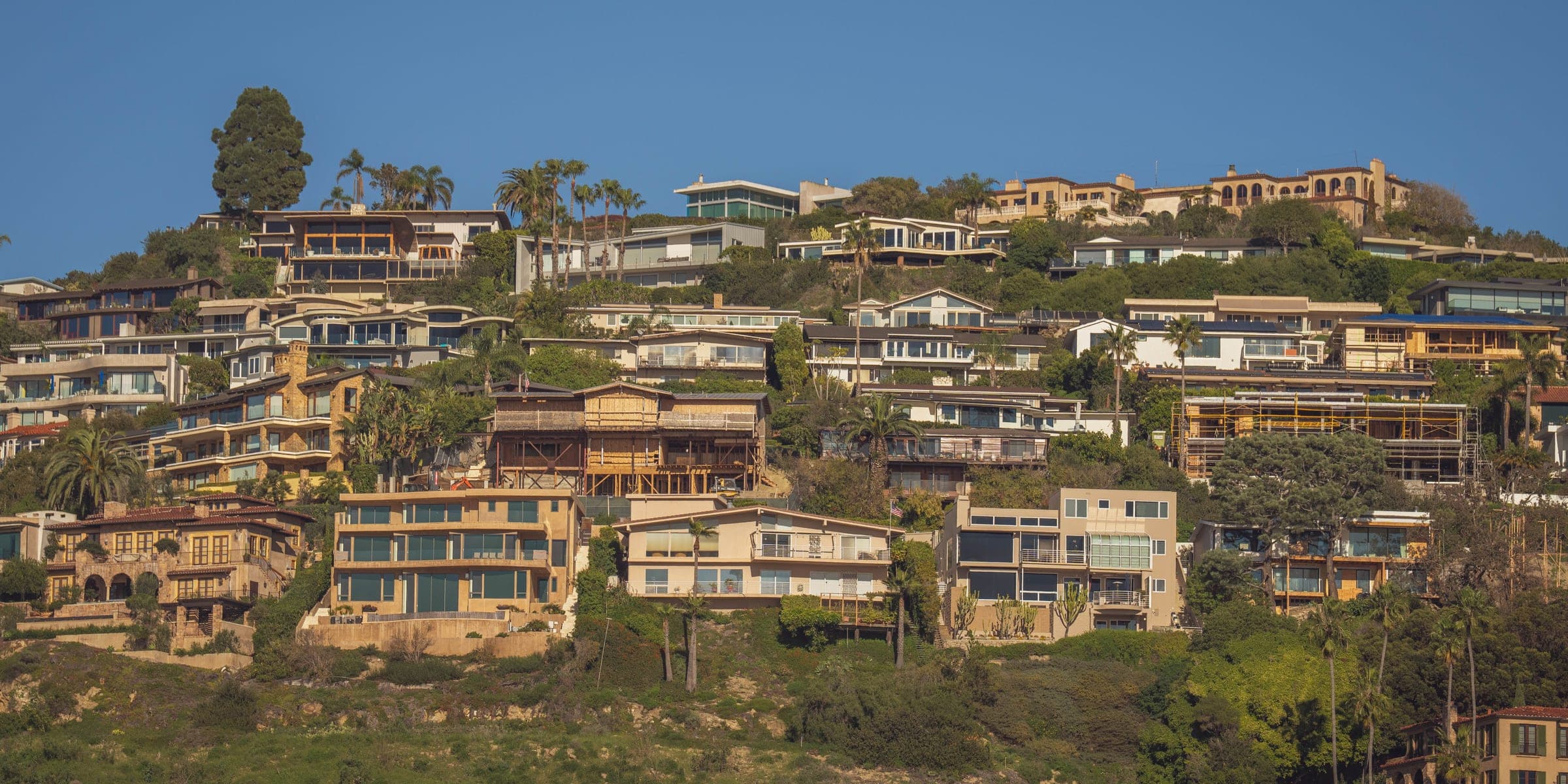 Terraced homes climbing a green hillside under a clear blue sky
