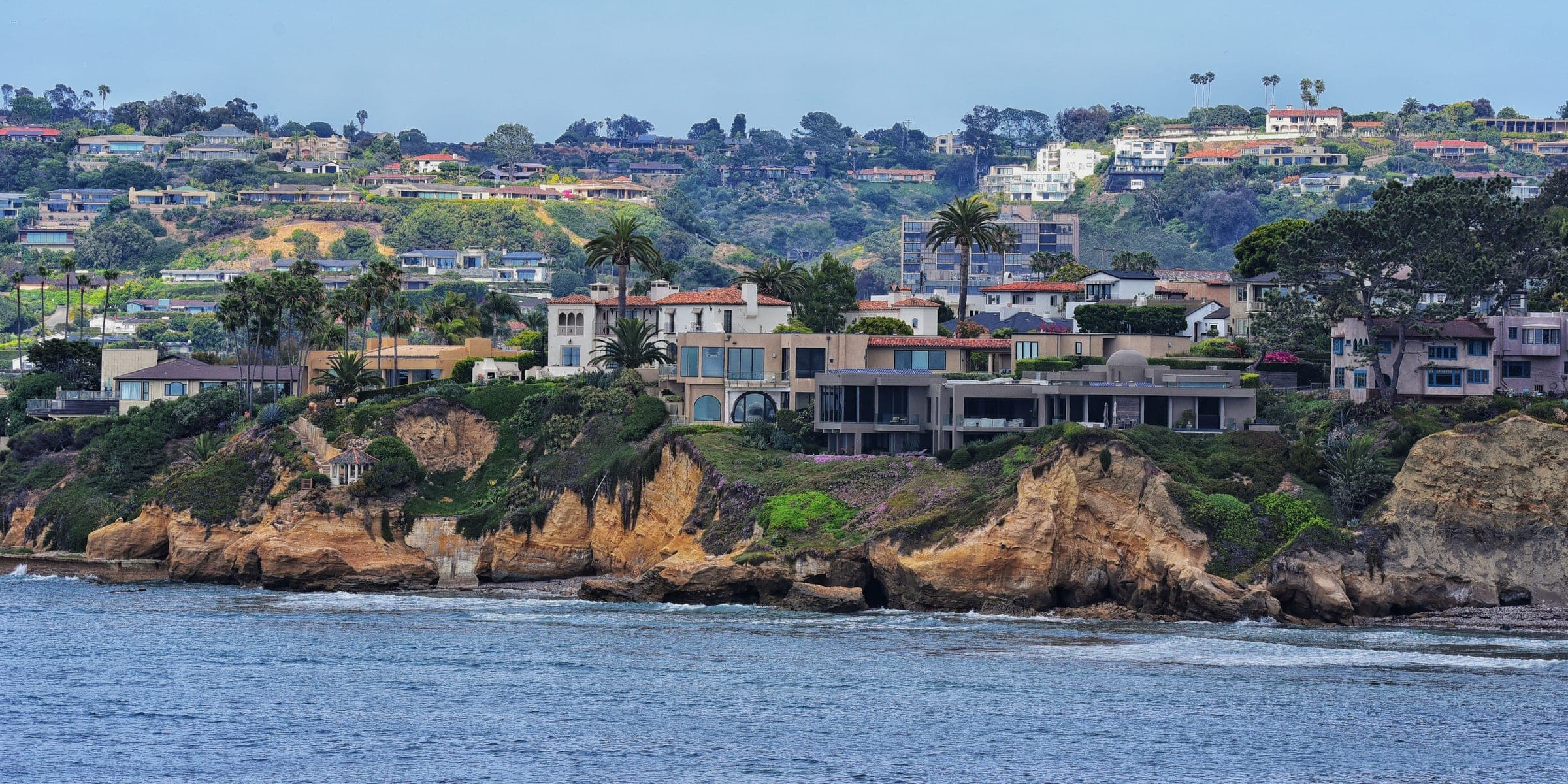 Homes on a green hillside above rocky coastal cliffs and the ocean