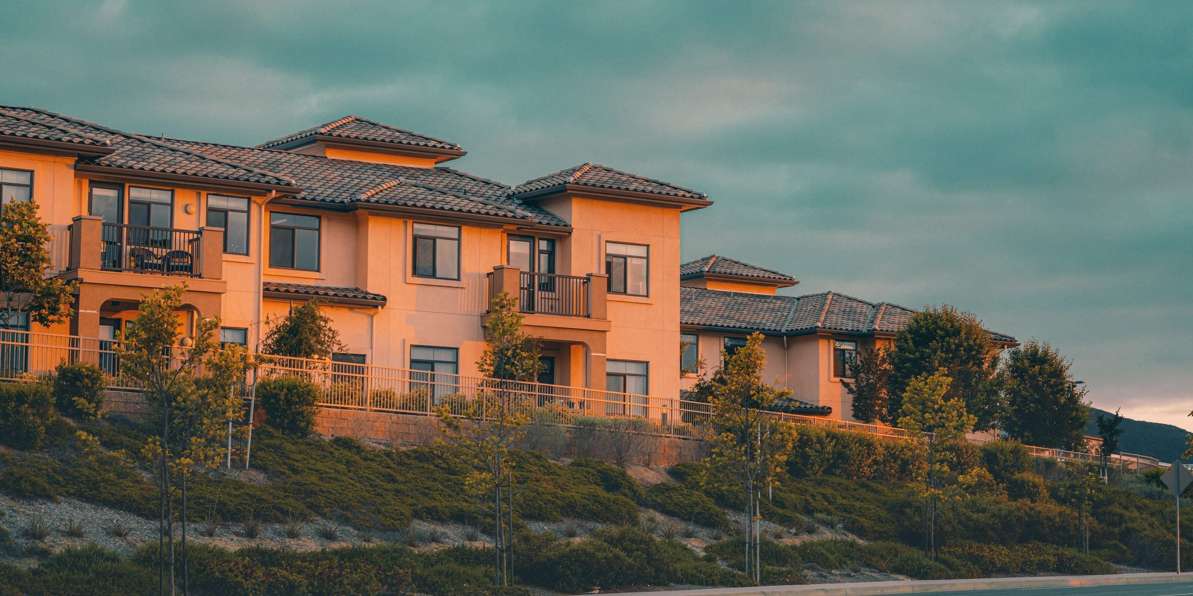 Row of peach stucco two-story homes with tile roofs on a landscaped slope at dusk