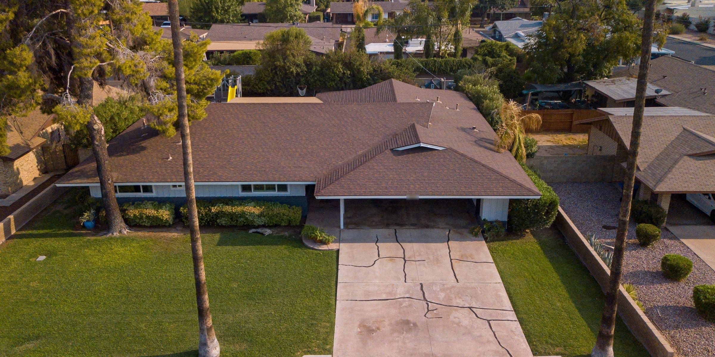 Aerial view of a single-story ranch house with a front lawn, palms and a driveway