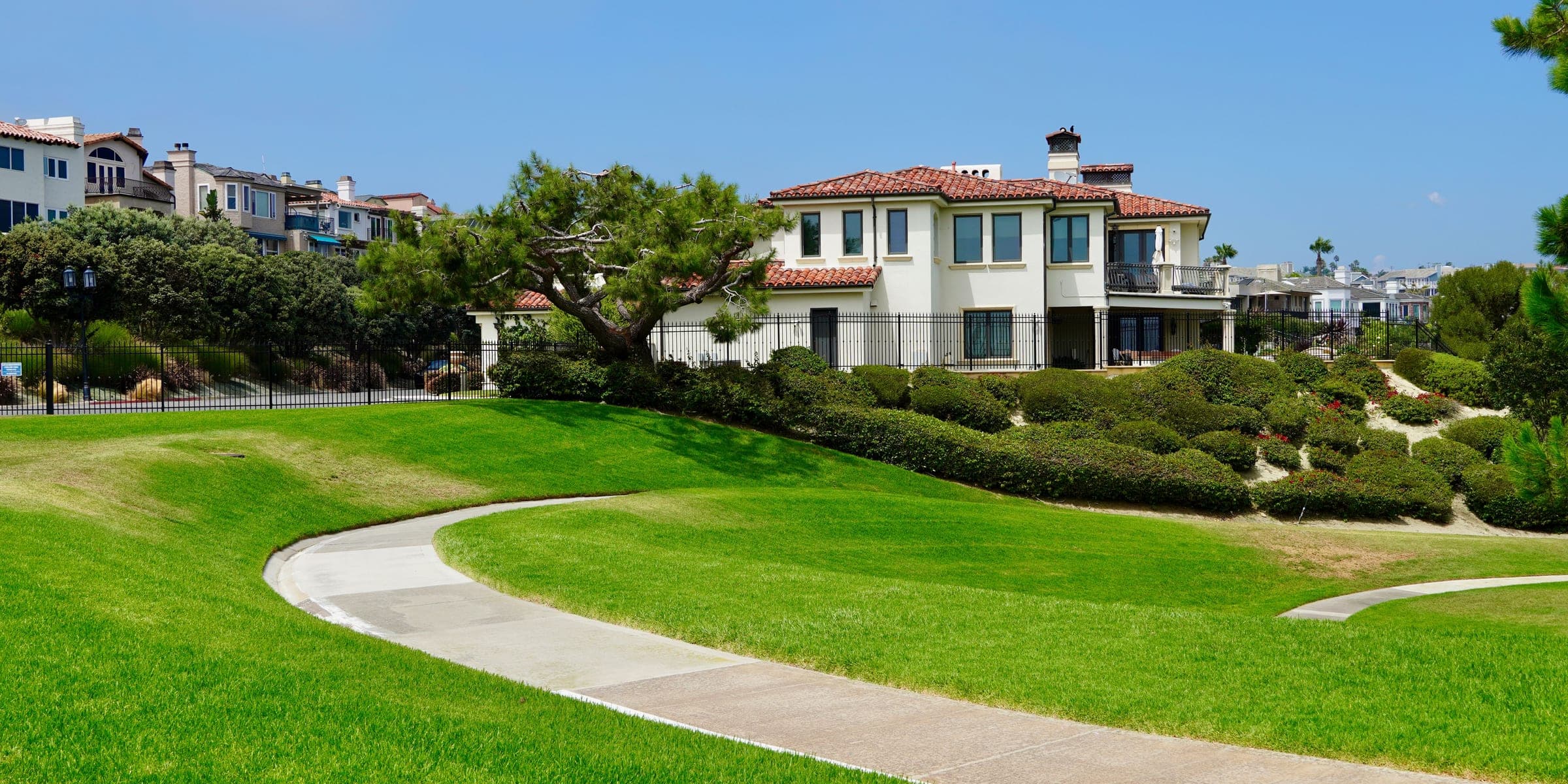 Two-story stucco house with a tile roof above a green park lawn and curving path