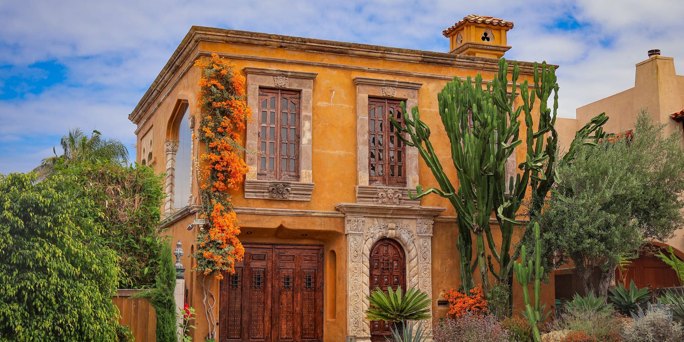 Ochre stucco Spanish style house with carved wood doors, cactus and a dry garden