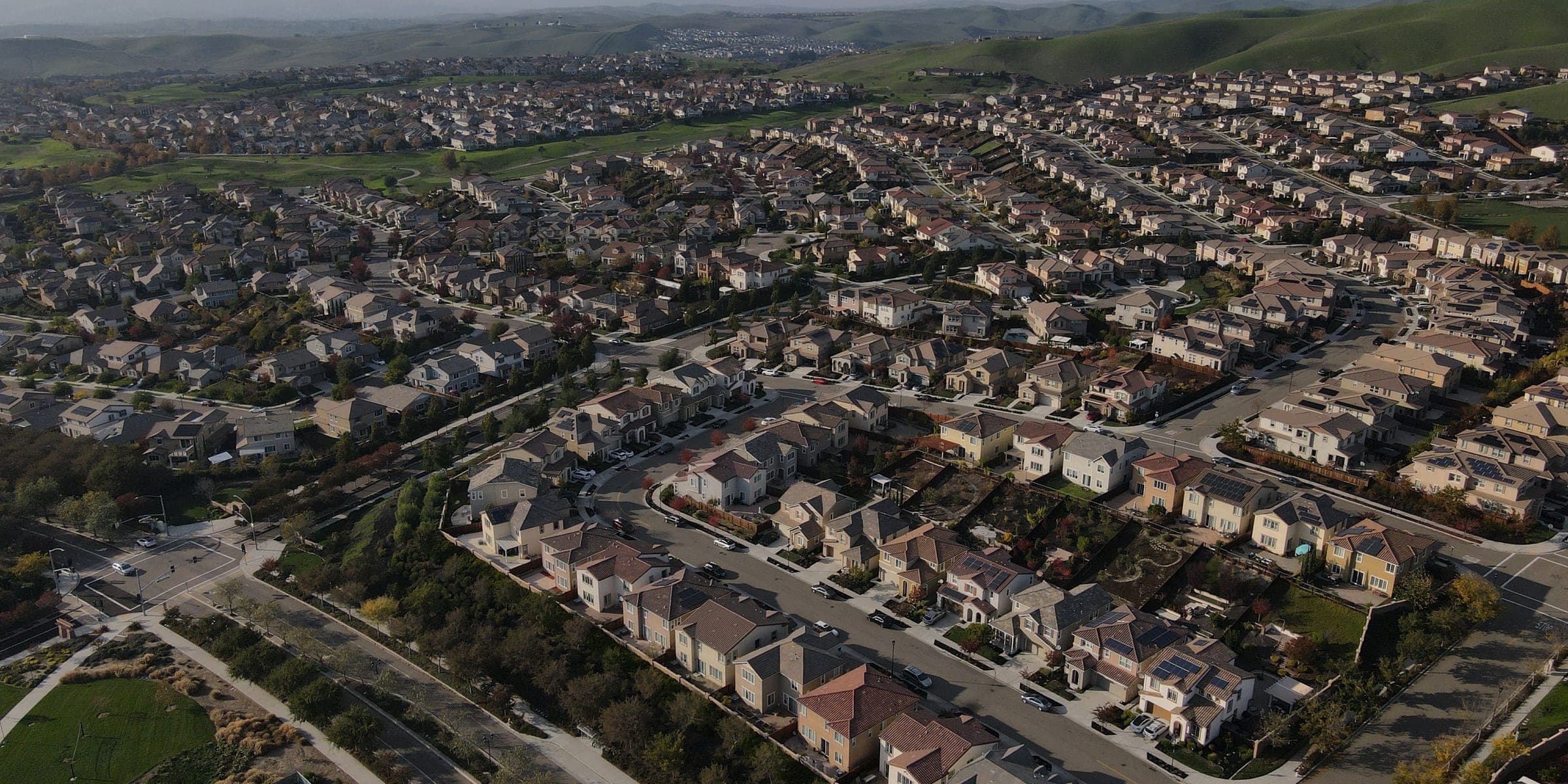 Aerial view of a planned neighborhood of two-story homes with curving streets, a park and green hills behind