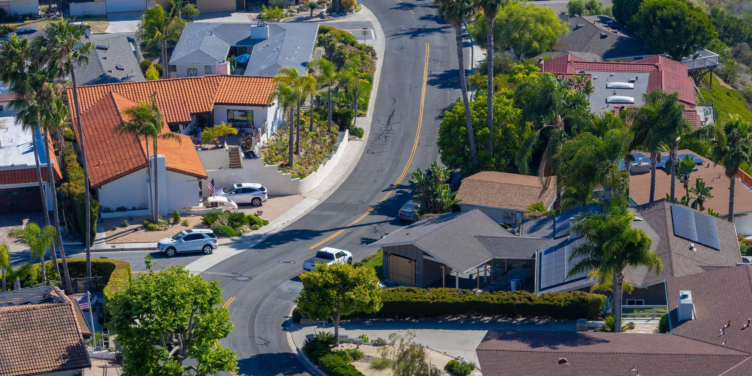 Aerial view of a curving street lined with tile and shingle roofed homes and palm trees