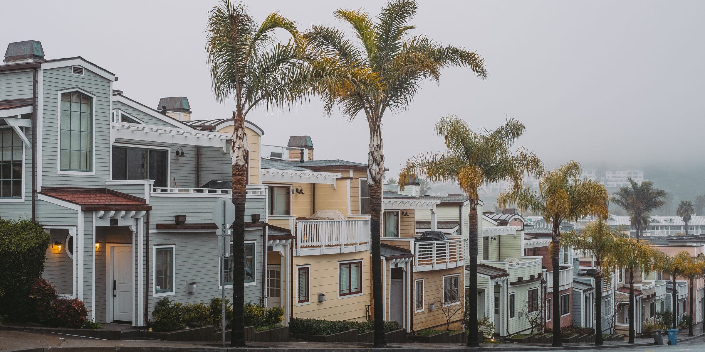 Row of two-story beach houses with balconies along a palm-lined street on an overcast morning