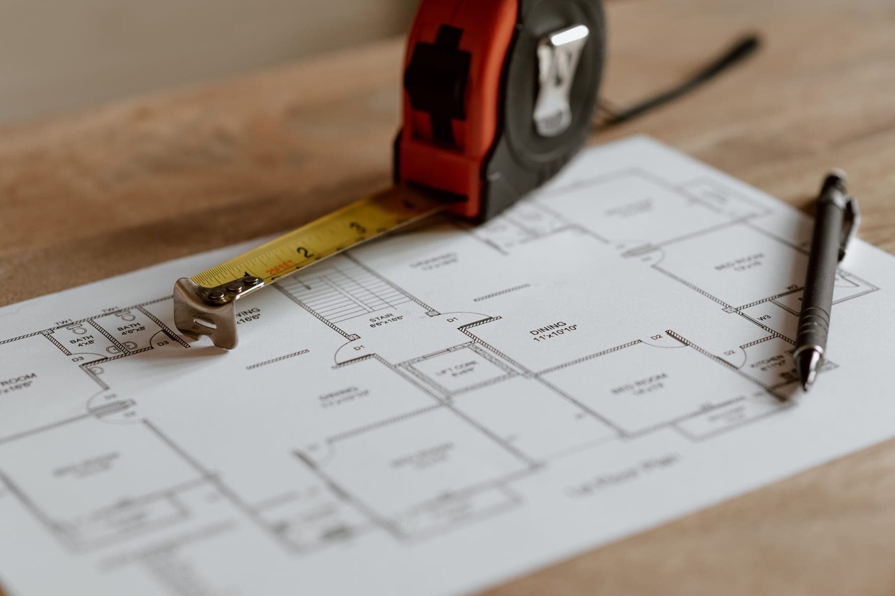 Tape measure and pen resting on a printed house floor plan