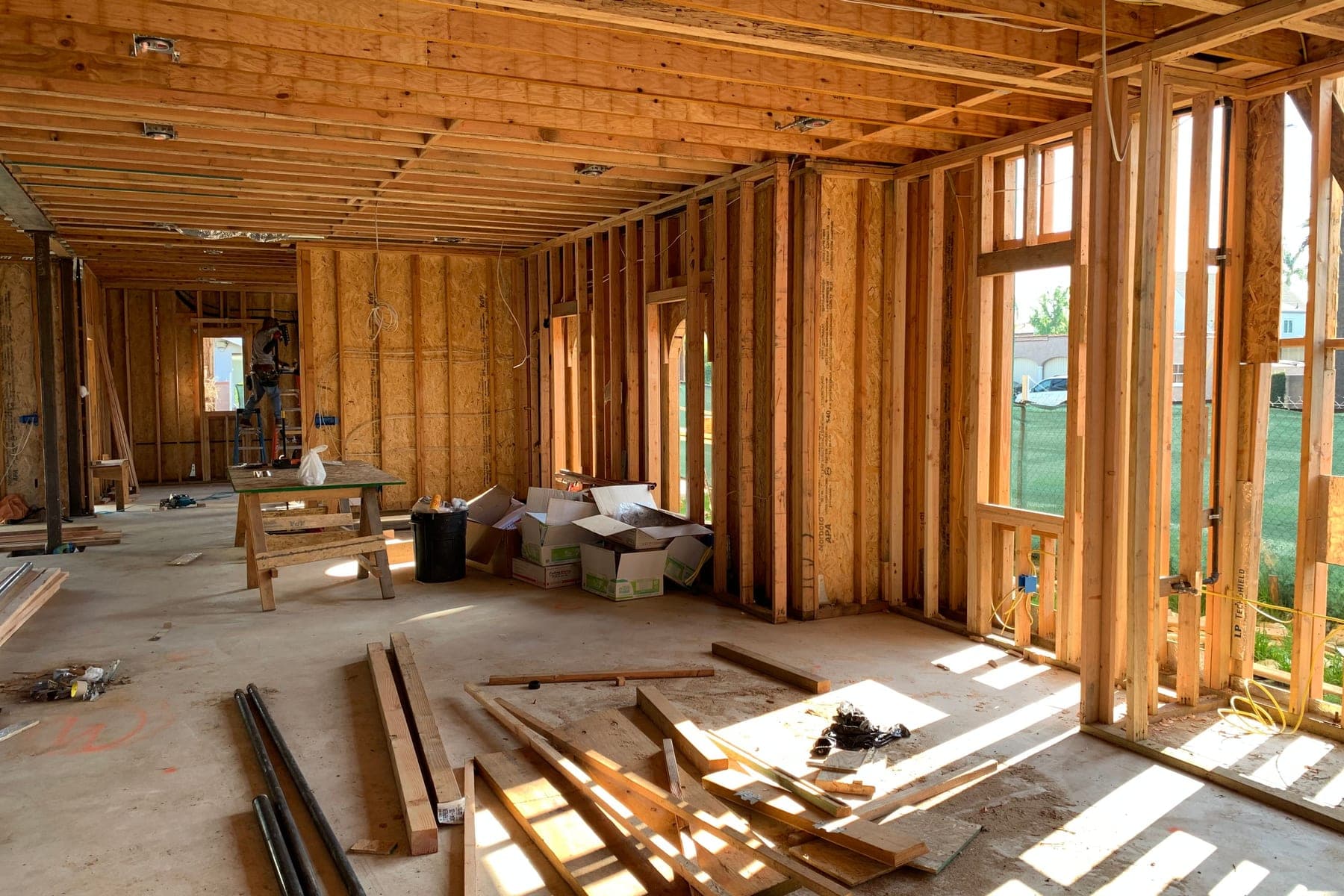 Sunlit interior with exposed wood studs and lumber on a concrete floor