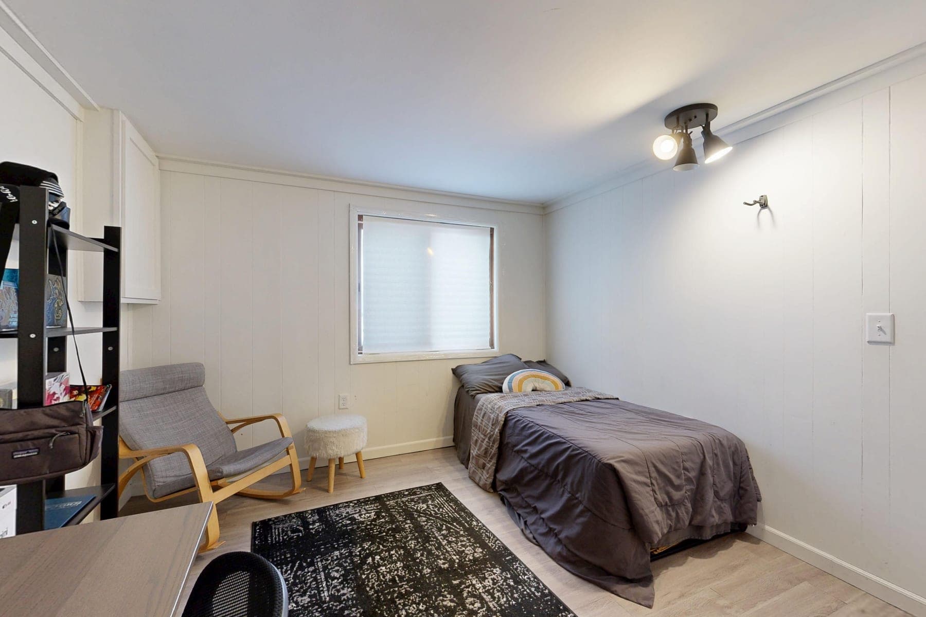 Small simply furnished bedroom with a twin bed, chair and paneled walls