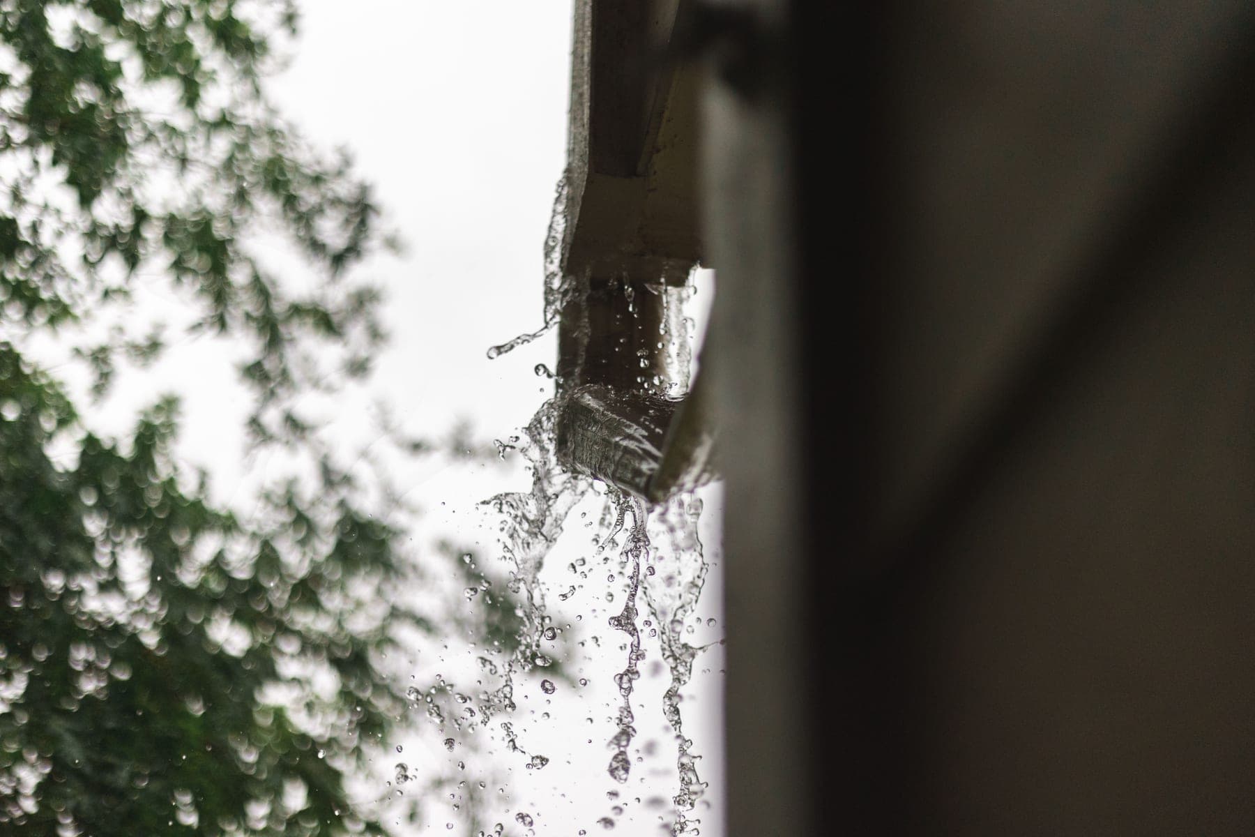 Rainwater spilling from the end of a roof gutter during a storm