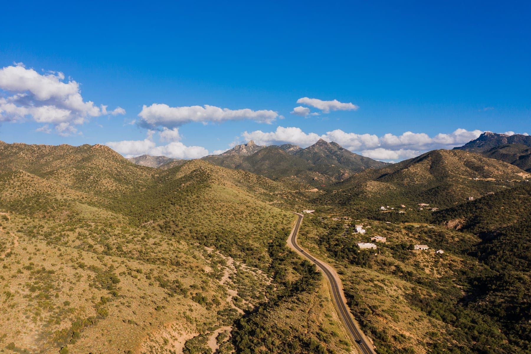 Aerial view of brush-covered hills and mountains with a winding road and a few scattered homes