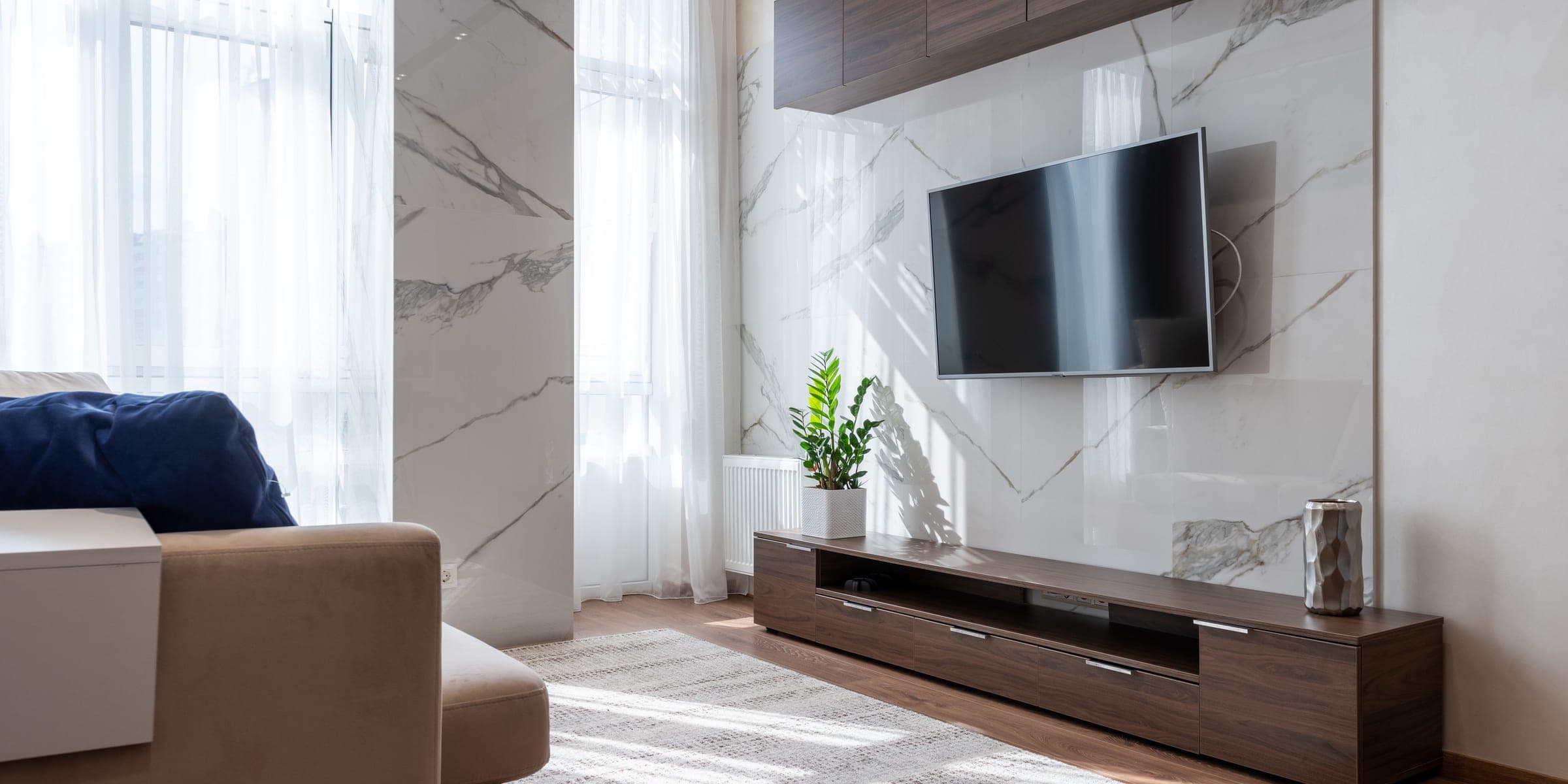 Flat screen TV mounted on a marble living room wall above a wooden console
