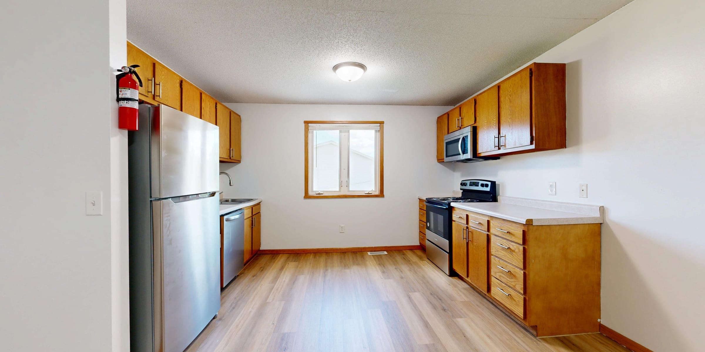 Fire extinguisher mounted on the wall by the refrigerator in an empty kitchen