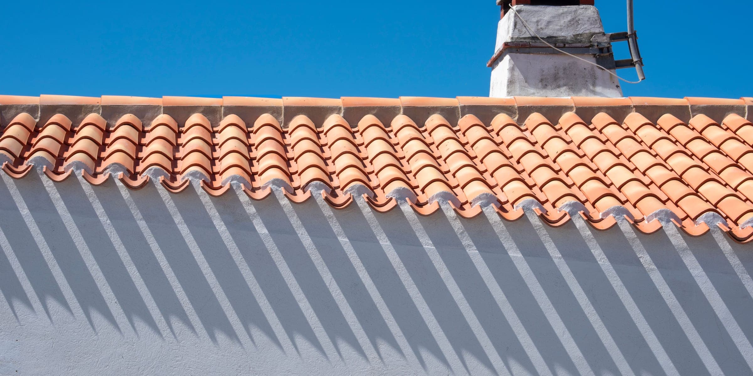 Orange clay tile roof and white chimney seen from below against a blue sky
