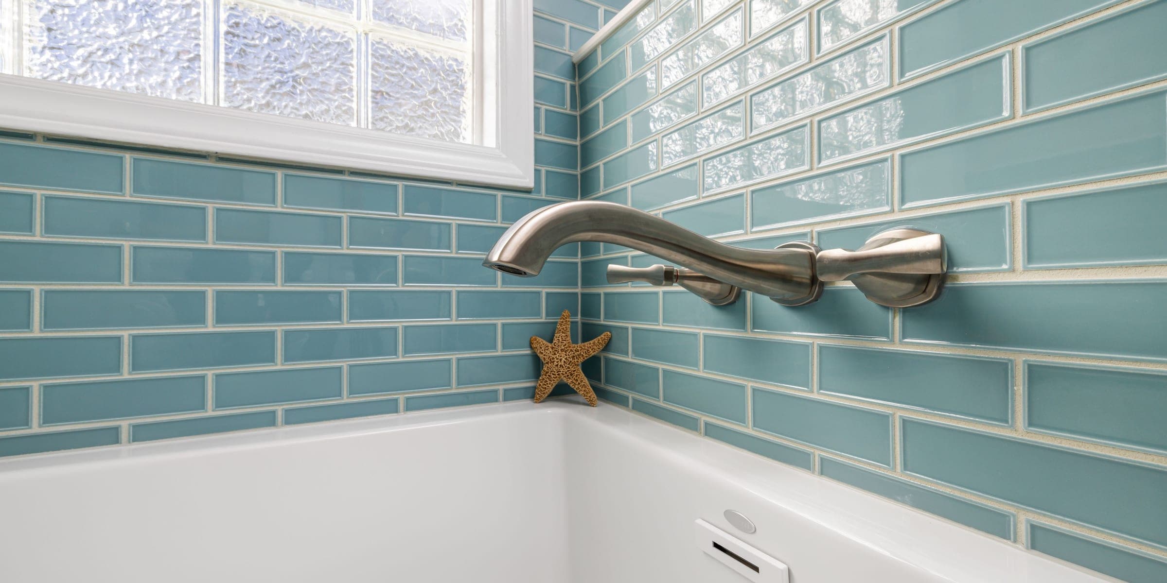 White bathtub meeting blue subway tile wall, showing the seam along the tub edge