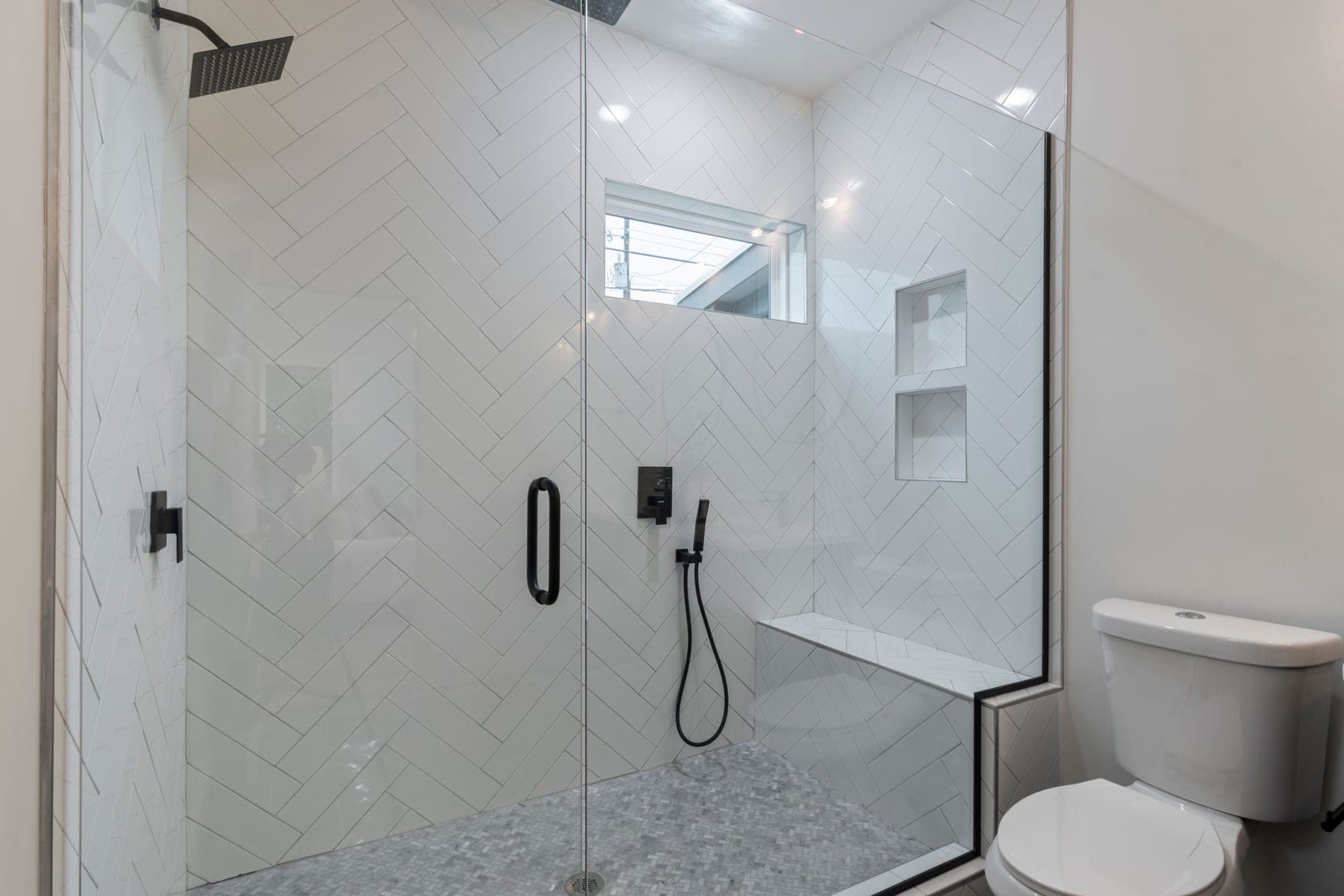 Bright bathroom with a glass walk-in shower, white herringbone tile and black fixtures