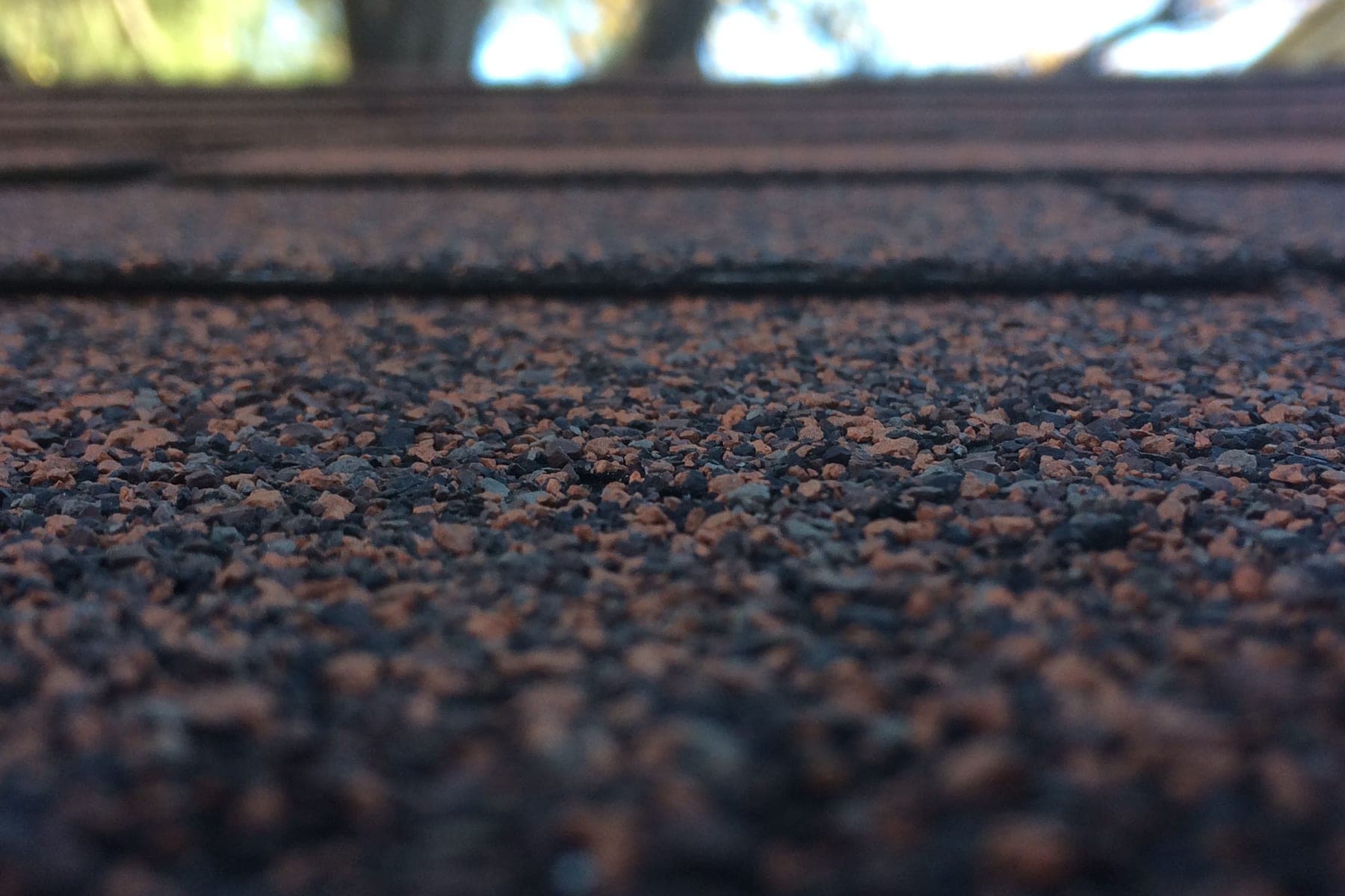 Low-angle close-up of dark brown asphalt roof shingles with shallow focus