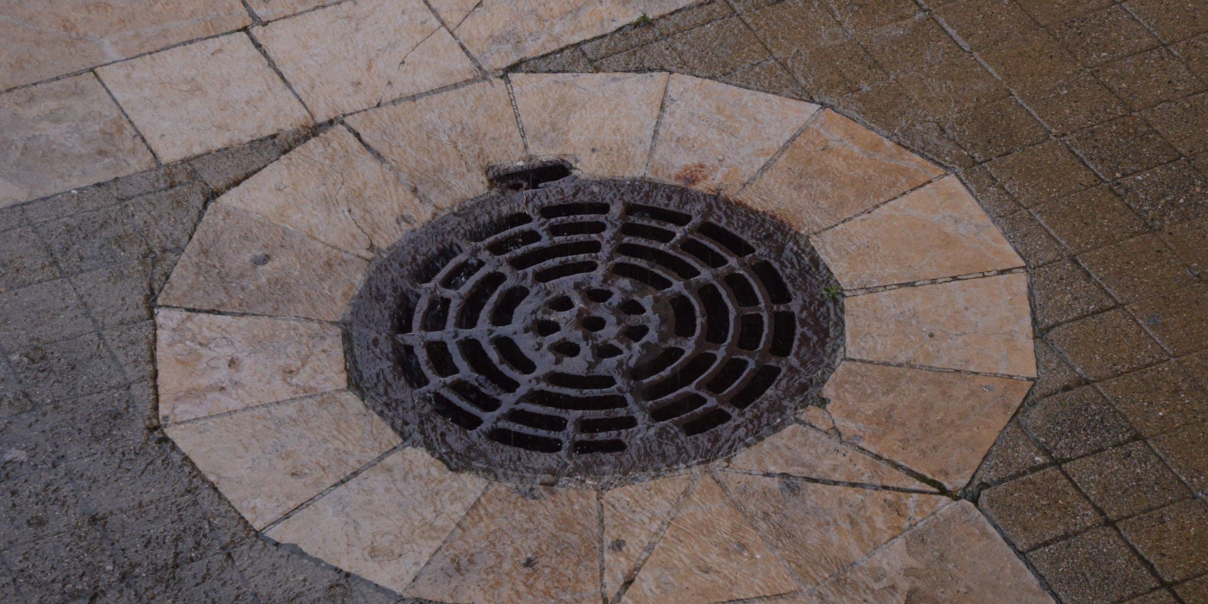 Round metal drain grate set into stone pavers